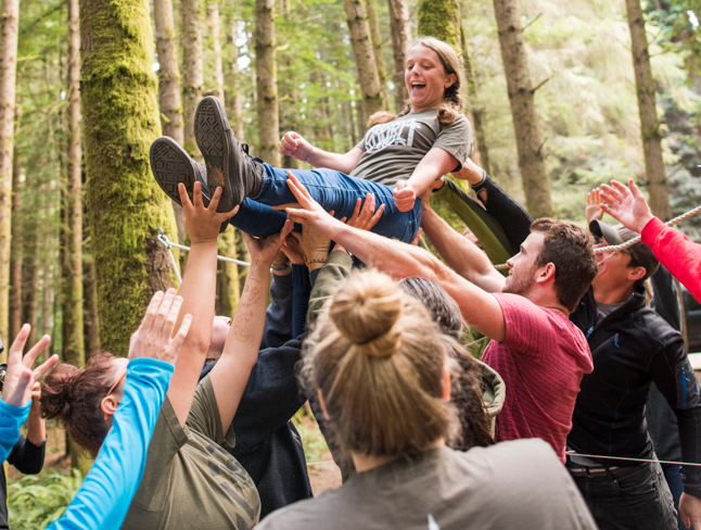 A photo of Cal Poly Humboldt students holding up another student in the forest.